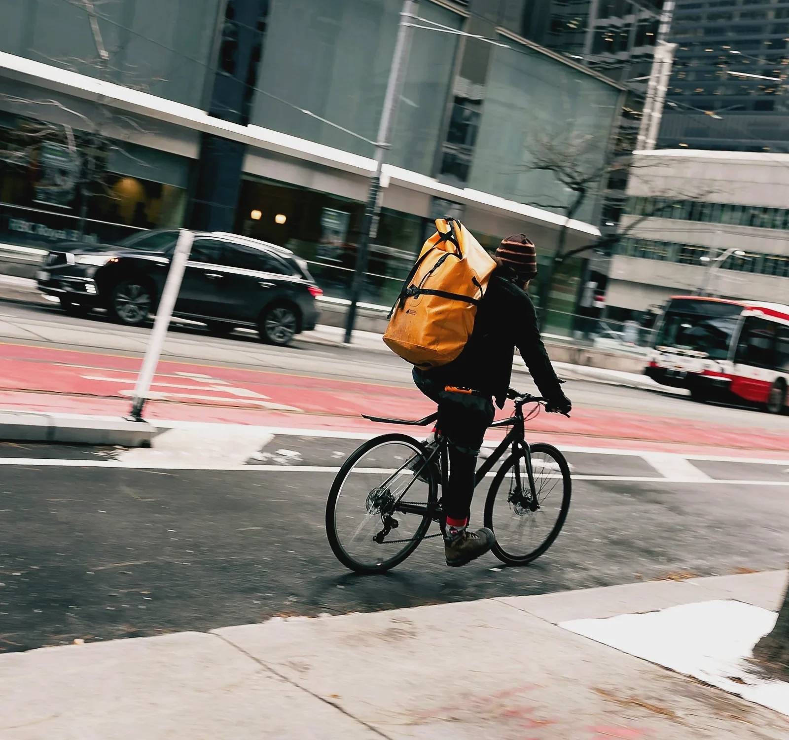 Swiftdrop rider with an orange courier bag cycling down a city bike lane
