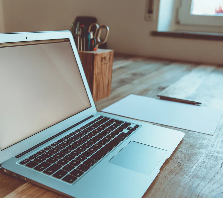 A laptop on a tidy wooden desk by a window on a quiet afternoon