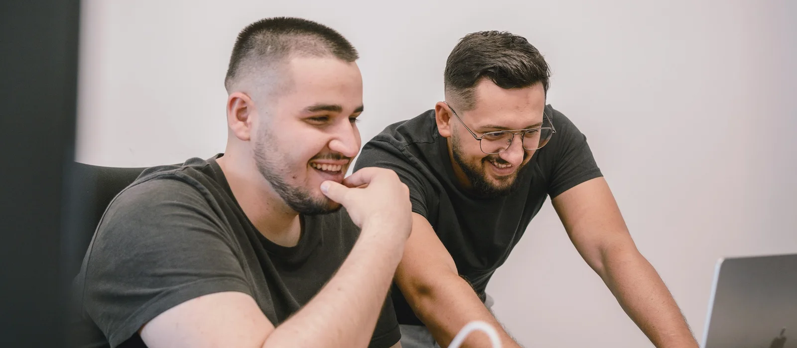 The two Fernbrook founders laughing over a laptop at their desk in Leeds